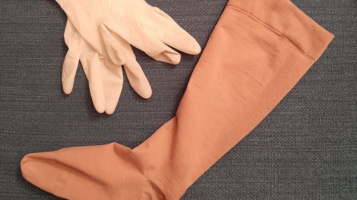 Kompressionsstrumpf liegt neben Einmalhandschuhen auf einem grauen Untergrund, bereit zum Anziehen.