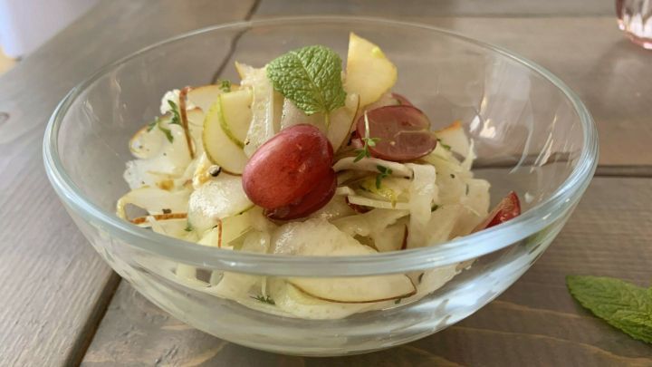 Ein frischer Birnen-Fenchel-Salat mit Trauben in einer Sch&uuml;ssel, serviert auf einem Holztisch.