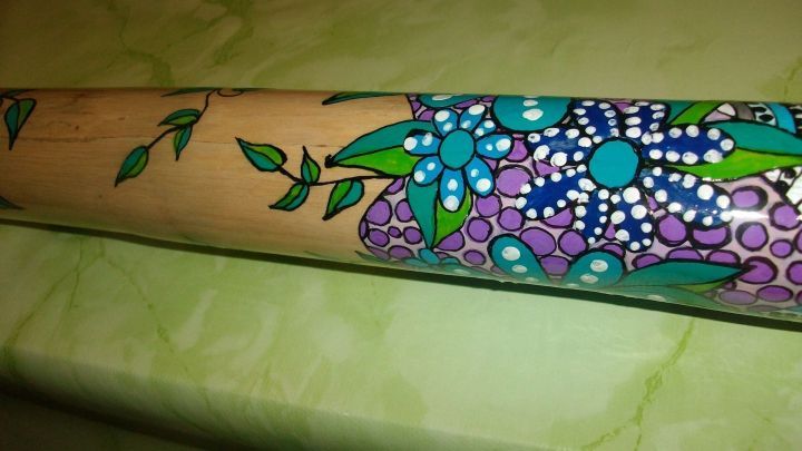 Ein bemaltes Didgeridoo mit bunten Acrylfarben liegt auf einem hellgr&uuml;nen Tisch und zeigt florale Designs.