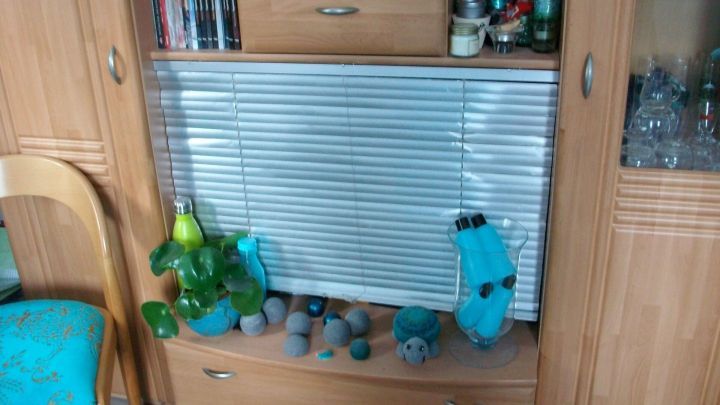 Ein Holzschrank enth&auml;lt B&uuml;cher und Deko, w&auml;hrend eine gr&uuml;ne Pflanze daneben steht und Stauraum bietet.