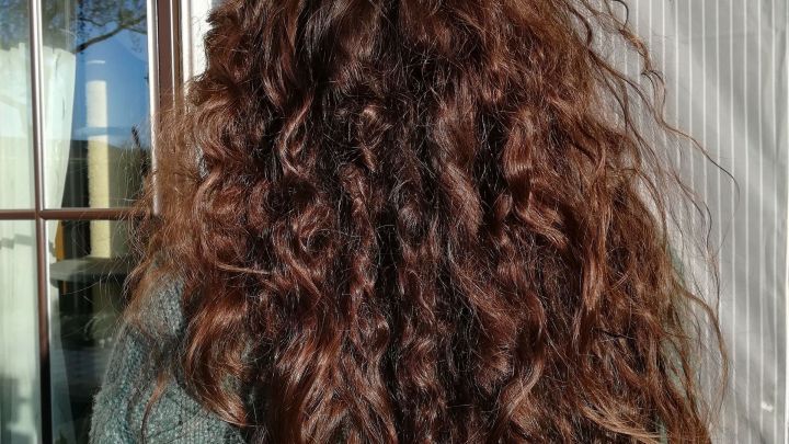 Lange, lockige Haare fallen auf die Schultern einer Person, die drau&szlig;en steht, im warmen Sonnenlicht.