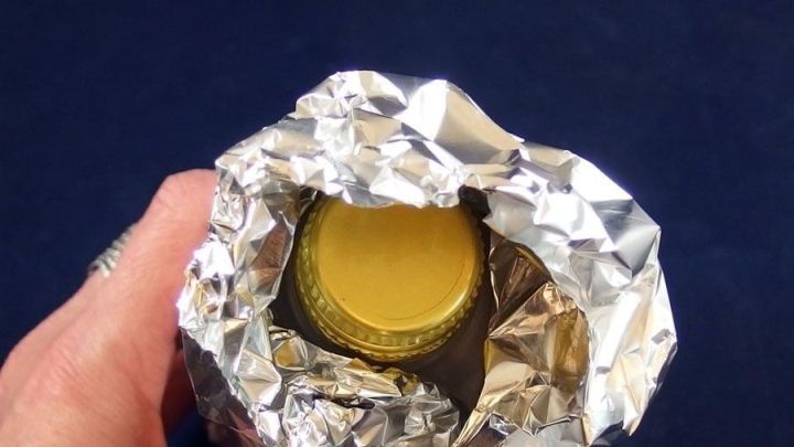 Ein Getr&auml;nk ist in Alufolie gewickelt, um es k&uuml;hl zu halten, w&auml;hrend eine Hand es in einem blauen Umfeld h&auml;lt.