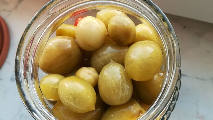 Unreife gr&uuml;ne Tomaten sind in einem Glas eingelagert, um zu fermentieren, auf einem hellen, glatten Untergrund.