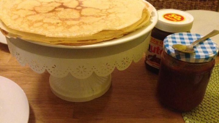 Ein Stapel fluffiger Pfannkuchen liegt auf einem Tortenst&auml;nder, daneben ein Glas Marmelade auf einem Holztisch.