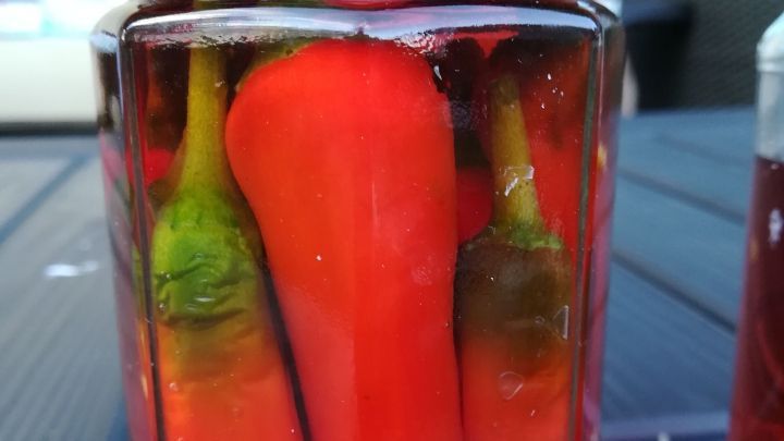 Eingelegte Chilis stehen in einem Glas mit Himbeeressig auf einem Tisch, umgeben von einem modernen, hellen Raum.