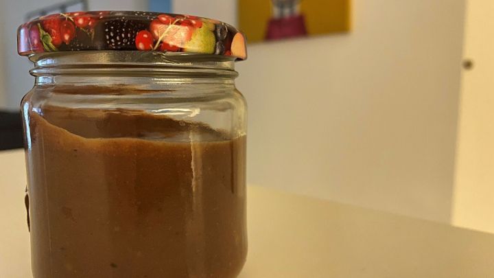 Ein Glas mit zuckerfreiem Schokoaufstrich aus Datteln steht auf einem Tisch in einem hellen Raum.