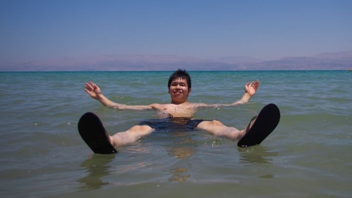 Ein Junge schwimmt entspannt im salzigen Wasser des Meeres unter klarem blauen Himmel, mit sanften Wellen um ihn herum.