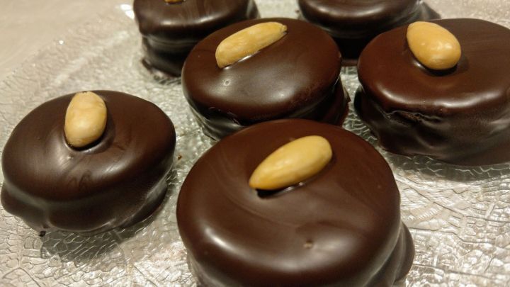 Schokoladen&uuml;berzogene Mozart-Taler mit Mandeln liegen dekorativ auf einem gl&auml;sernen Teller.