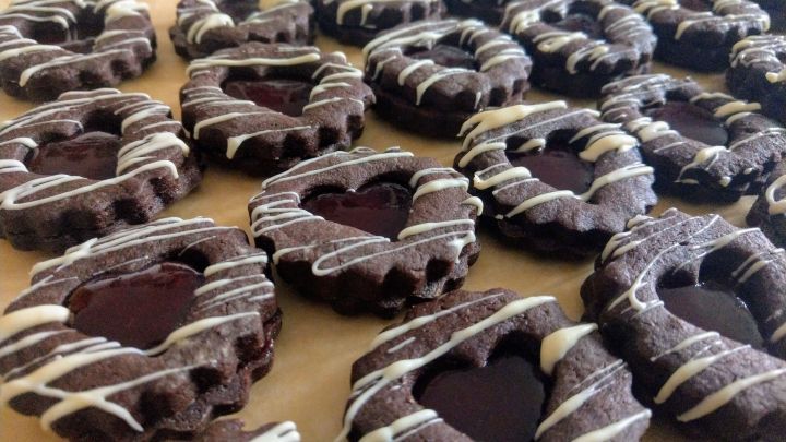 Kekse mit einem herzf&ouml;rmigen Loch werden mit Schokoladendekoration auf einer braunen Unterlage pr&auml;sentiert.