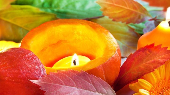 Ein K&uuml;rbis mit einer Kerze innen leuchtet zwischen bunten Bl&auml;ttern und gelben Blumen in einer herbstlichen Dekoration.