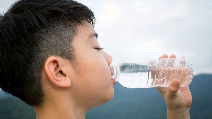 Ein Junge trinkt aus einer PET-Flasche, umgeben von einer nat&uuml;rlichen Landschaft mit H&uuml;geln und leichtem Himmel.
