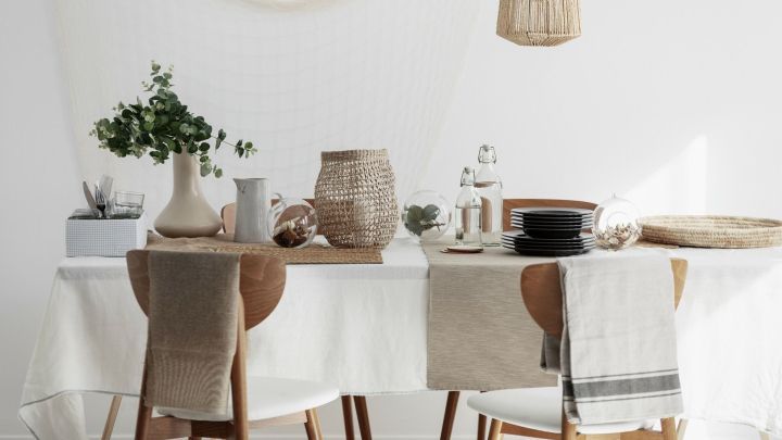 Ein eleganter Tisch mit einer wei&szlig;en Tischdecke und Naturaccessoires wird geschm&uuml;ckt von Blumen und Glasobjekten.