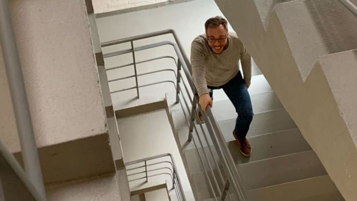 Ein Mann l&auml;chelt und h&auml;lt sich an einem Treppengel&auml;nder fest, w&auml;hrend er eine Treppe hinaufsteigt.