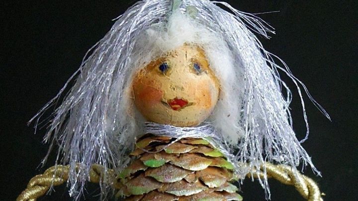 Ein Engel aus Tannenzapfen mit goldenen Fl&uuml;geln steht vor schwarzem Hintergrund und strahlt festlichen Charme aus.