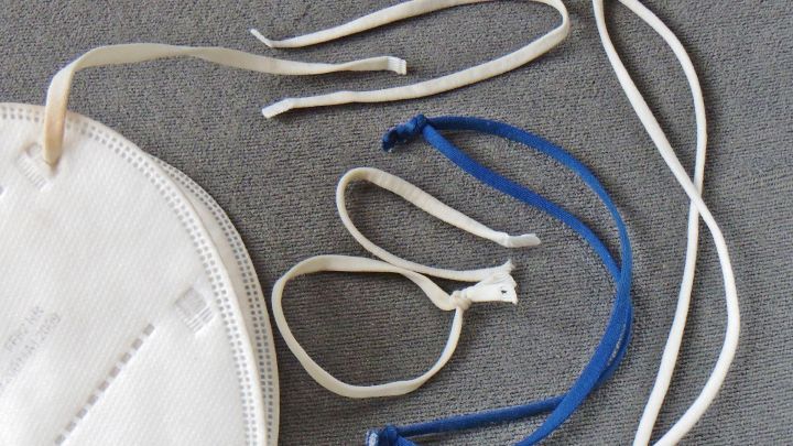 Eine FFP2-Maske liegt auf einem grauen Untergrund, umgeben von verschiedenen Gummib&auml;ndern zum Wiederverwenden.