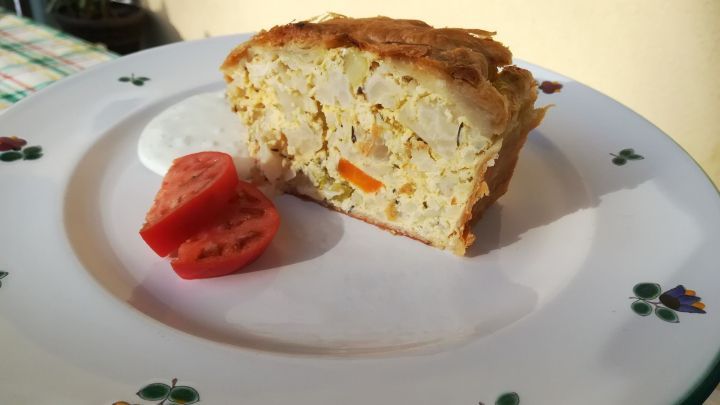 Saftiger Blumenkohlstrudel liegt auf einem dekorativen Teller, begleitet von Tomatenscheiben und Knoblauch-Dip.