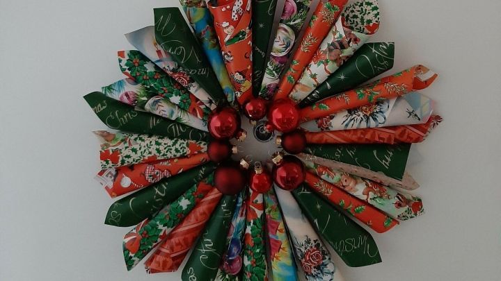 Ein bunter Weihnachtskranz aus Papierrollen und roten Kugeln h&auml;ngt an einem roten Band an der Wand.