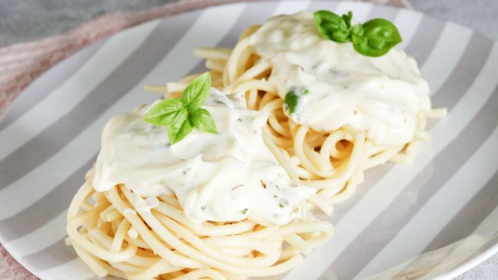 Zwei Portionen Spaghetti mit cremiger Sauce, garniert mit frischem Basilikum, auf einem gestreiften Teller.