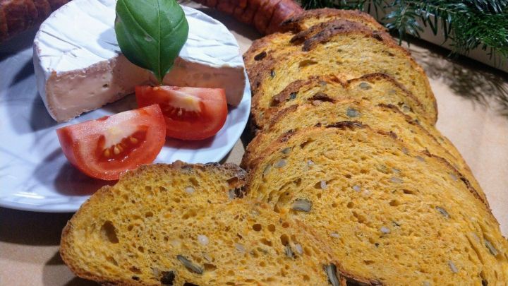 K&uuml;rbisbrot liegt neben einem K&auml;se und Tomatenscheiben auf einem Teller, umgeben von Wurst und festlichem Dekor.