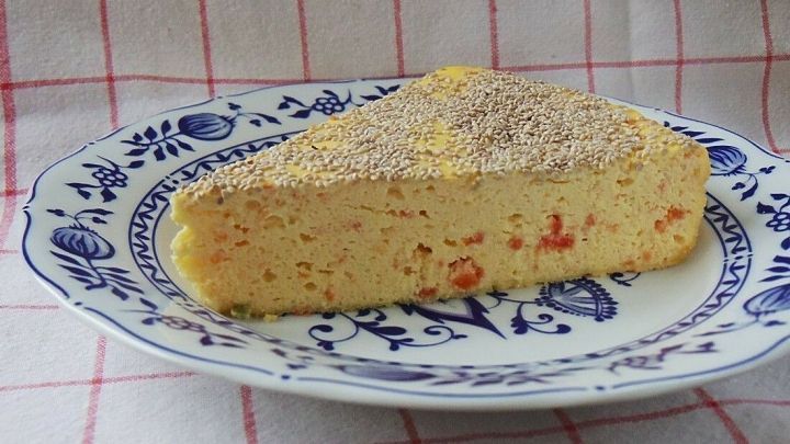Ein St&uuml;ck k&auml;sekuchen ist auf einem blauen, gemusterten Teller angerichtet. Das Desserts mit Tomaten und Chia-Samen steht vor einem karierter Tischdecke.