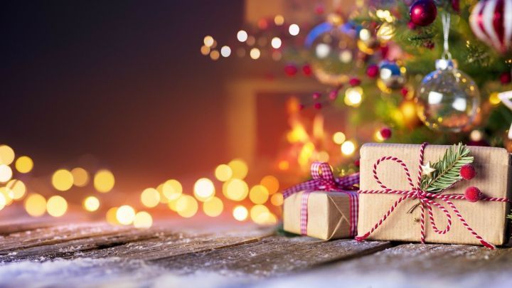 Festlich dekorierte Geschenke liegen auf einem Holztablett, umgeben von einem Weihnachtsbaum und warmen Lichtern.