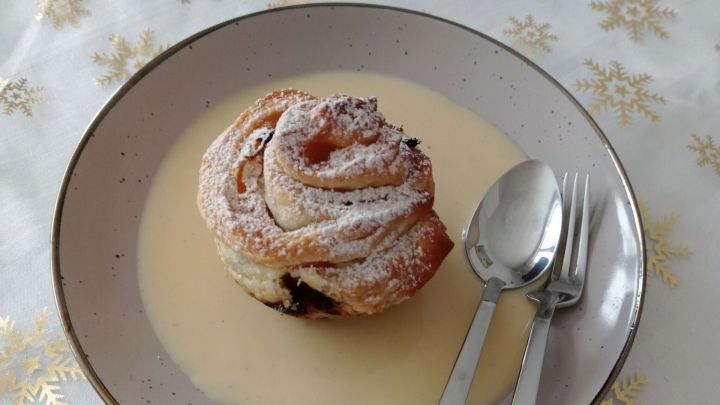 Bl&auml;tterteigrosen liegen auf einem Teller mit Vanilleso&szlig;e, umgeben von einem festlichen, goldenen Tischdecke.