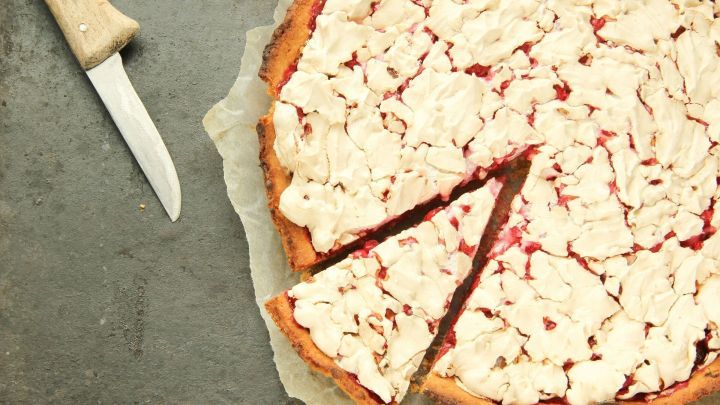 Ein Tr&auml;ubleskuchen mit Baiser liegt auf einem Backpapier, ein St&uuml;ck ist herausgeschnitten, daneben ein Messer.