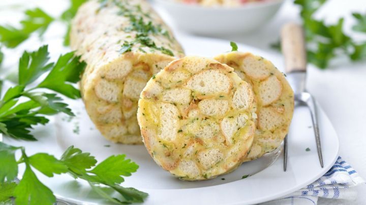 Serviettenkn&ouml;del, auf einem Teller angerichtet, mit frischen Kr&auml;utern garniert, liegt neben einer Gabel und einem Messer.