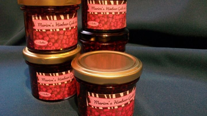 F&uuml;nf Gl&auml;ser Himbeerkonfit&uuml;re stehen auf einem blauen Hintergrund, dekoriert mit gestreiften Etiketten und goldenen Deckeln.