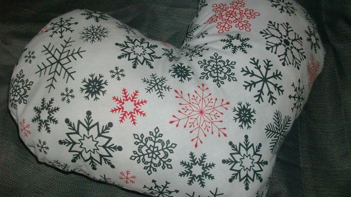 Ein Herz-Kissen mit Schneeflocken-Muster liegt auf einem dunklen, strukturierten Hintergrund.