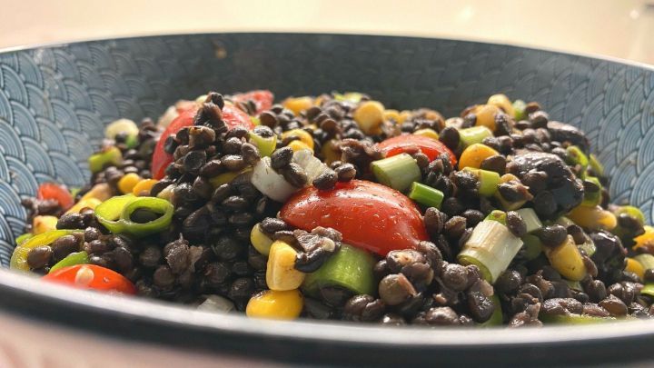 Ein bunter Salat aus Belugalinsen und Mais mit frischen Tomaten und Fr&uuml;hlingszwiebeln in einer dekorativen Sch&uuml;ssel.