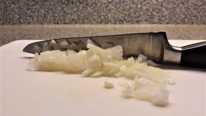 Ein scharfes Messer liegt auf einem Schneidebrett, umgeben von fein gehackten Zwiebelst&uuml;cken.