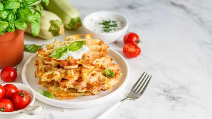 Goldene Pizzawaffeln liegen auf einem Teller, garniert mit frischem Basilikum, umgeben von Tomaten und Dip.