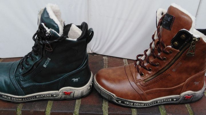 Schwarze und braune Stiefel stehen nebeneinander auf einem Boden, bereit zum Reinigen von Impr&auml;gnierspray-Flecken.