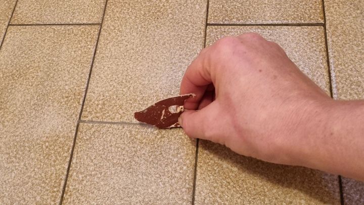 Ein Handwerker reinigt eine schmutzige Fuge mit Schleifpapier auf einem gefliesten Boden in einem Wohnraum.