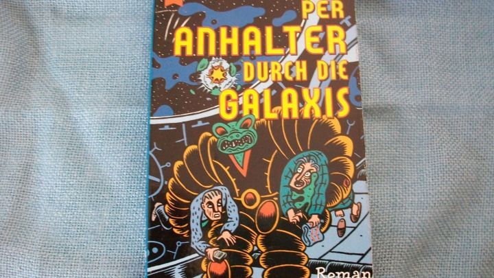 Ein buntes Buchcover zeigt den Titel &bdquo;Per Anhalter durch die Galaxis&ldquo; &uuml;ber einer fantasievollen Darstellung von Charakteren im Weltraum.