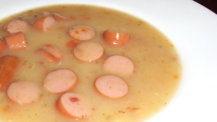 Ein cremiger Eintopf aus p&uuml;rierter Br&uuml;he mit Scheiben von W&uuml;rstchen schwimmt in einer wei&szlig;en Sch&uuml;ssel.