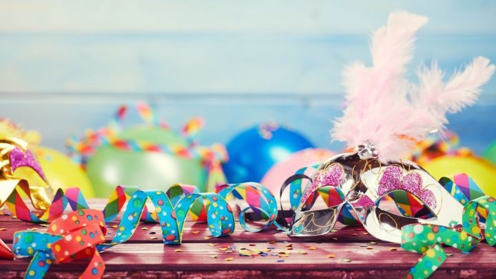 Bunte Masken und Luftschlangen liegen auf einem Tisch, umgeben von festlichen Ballons &ndash; eine fr&ouml;hliche Faschingsfeier-Stimmung.
