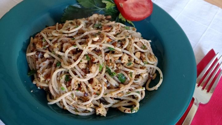 Ein Teller mit Spaghetti, garniert mit Waln&uuml;ssen und Tomate, liegt auf einem Tisch mit roter Serviette und Besteck.