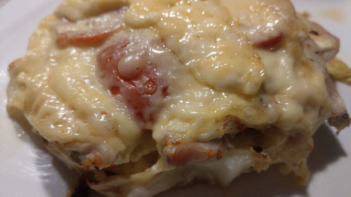 Ein &uuml;berbackenes Huhn liegt auf einem Bett aus Kohl, bedeckt mit geschmolzenem K&auml;se und speckigen Tomatenscheiben.