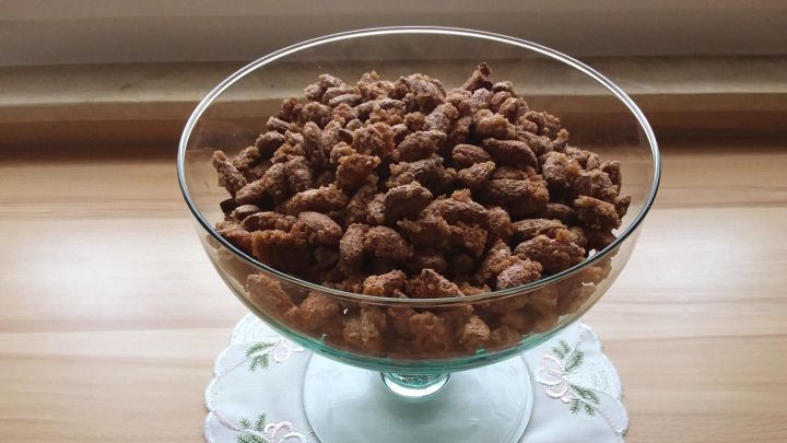 Eine gro&szlig;e Glassch&uuml;ssel enth&auml;lt gebrannte Mandeln, die auf einem h&uuml;bschen, bestickten Tischset stehen.