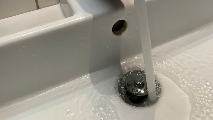 Ein gl&auml;nzender Wasserhahn l&auml;sst Wasser in ein Waschbecken laufen, w&auml;hrend die flie&szlig;ende Str&ouml;mung auf der Wasseroberfl&auml;che spritzt.