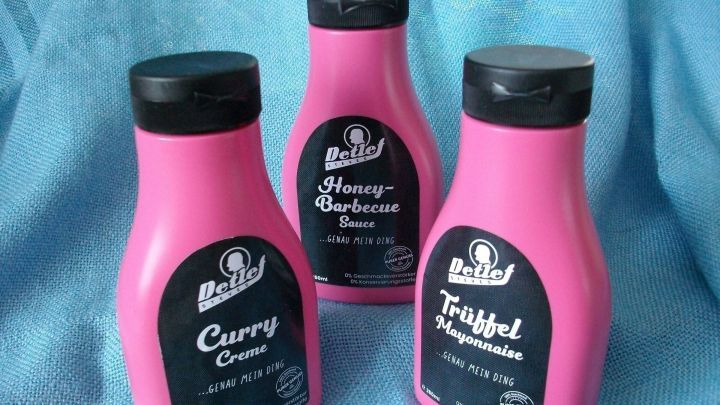 Drei pinke Flaschen stehen nebeneinander, gef&uuml;llt mit verschiedenen Grillso&szlig;en von Detlef Steves auf einem hellen Hintergrund.