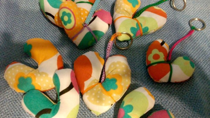 Bunte Herz-Schl&uuml;sselanh&auml;nger liegen auf einem blauen Tuch und sind farbenfroh gen&auml;ht, bereit zum Verschenken oder Verwenden.