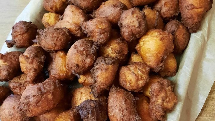 Knusprige Feuerspatzen aus Hefeteig liegen warm auf Papier in einem Blech, umgeben von einem holzfarbenen Tisch.