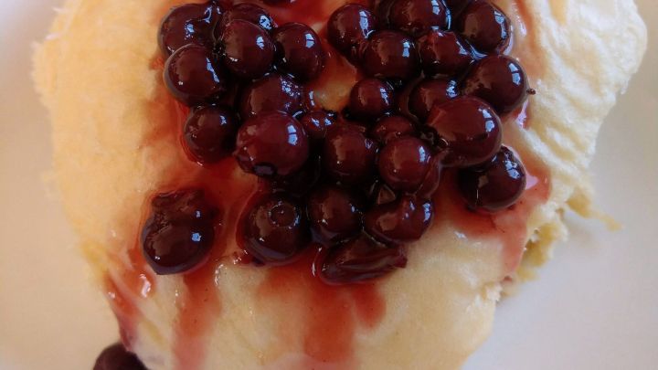 Dinkel Hefekl&ouml;&szlig;e liegen auf einem Teller und sind mit dunklen Beeren und roter Sauce garniert.