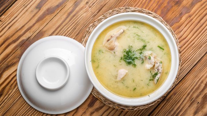 Eine cremige Gefl&uuml;gelsuppe in einer wei&szlig;en Sch&uuml;ssel, serviert auf rustikalem Holz, mit frischen Kr&auml;utern garniert.