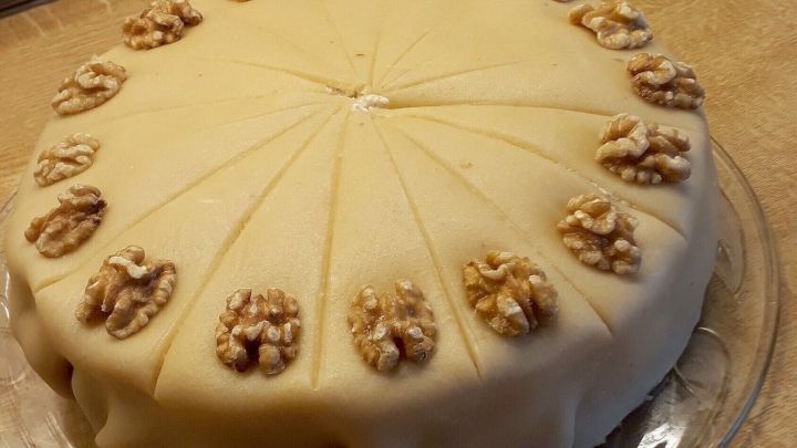 Eine runde Marzipan-Nuss-Torte liegt auf einem durchsichtigen Teller und ist mit Waln&uuml;ssen dekoriert, ideal f&uuml;r Ostern.