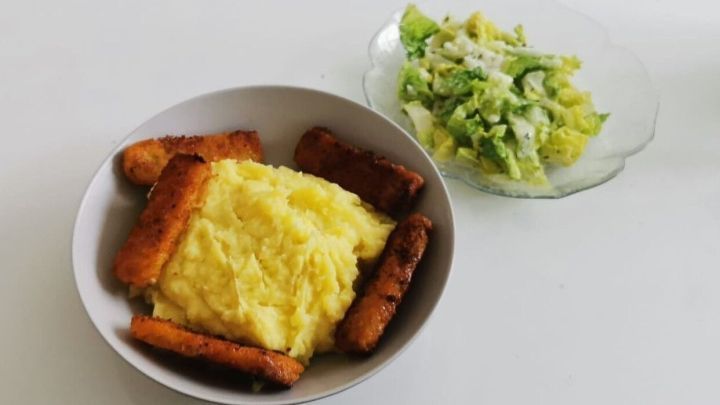 Ein Teller mit Kartoffelp&uuml;ree, umgeben von knusprigen St&auml;bchen und einem frischen Salat auf einem Tisch.