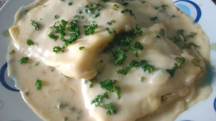 Zwei gef&uuml;llte Teigtaschen liegen in einer cremigen So&szlig;e, garniert mit frischem Gr&uuml;n, auf einem runden Teller.